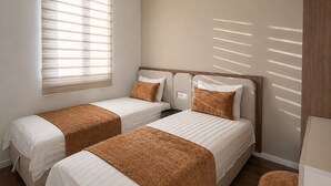 A hotel room with two beds, a window with blinds, a wardrobe, and a round wicker chair. - Guest House Fjola (Donji Štoj)