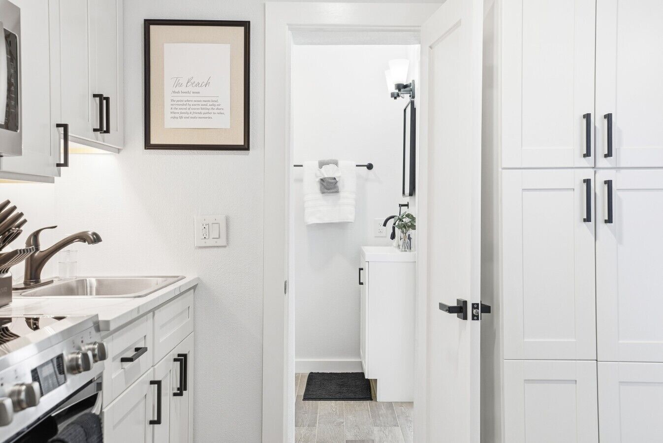 A modern kitchen with white cabinets, stainless steel appliances, and a framed quote on the wall.