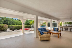 An outdoor covered patio area with wicker furniture, a pool, and a view of the surrounding greenery. - Salty Skies : 4-bedroom - Pool - Dock - walking distance from Sombrero Beach (Marathon)