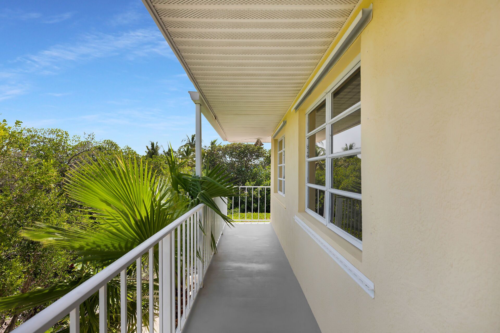 A covered balcony with a railing, a window, and a view of greenery.