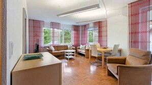A modern living room with a sofa, a dining table, and a chair. There are large windows with curtains. - Quiet Riverside Wallbach Apartment with Terrace, AC, Washer, and Rhine View (Bad Säckingen)