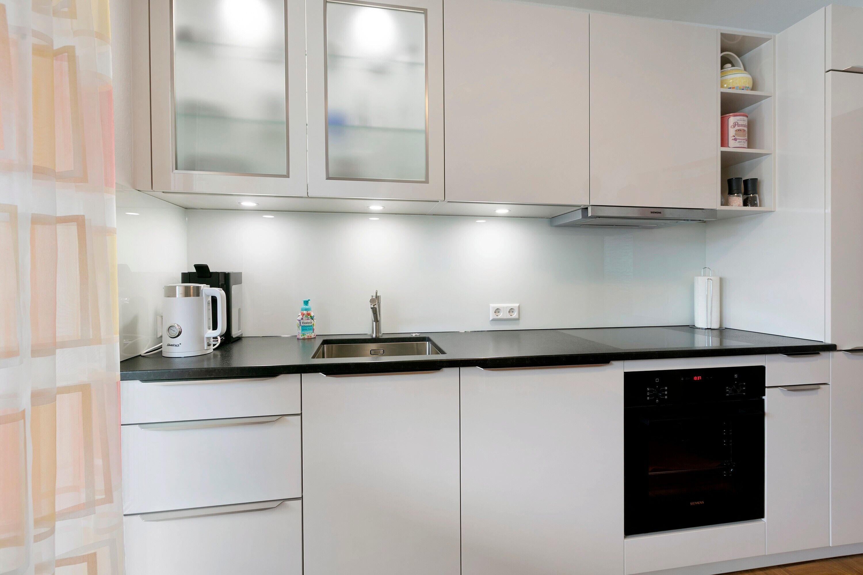 Eine moderne Küche mit weißen Schränken, einer schwarzen Arbeitsplatte, einem eingebauten Geschirrspüler und einem Siemens-Backofen.