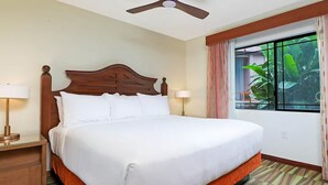 Hotellihuone, jossa on suuri sänky, kaksi yöpöytävalaisinta, kattotuuletin, ikkuna verhoilla ja puinen työpöytä.