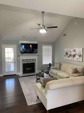 Ein Wohnzimmer mit Kamin, einem darüber montierten Fernseher, einem Deckenventilator und einem Sofa.