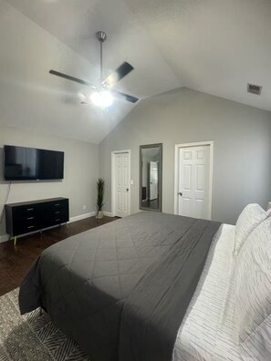 Ein Schlafzimmer mit Bett, Deckenventilator, Fernseher und Kommode.