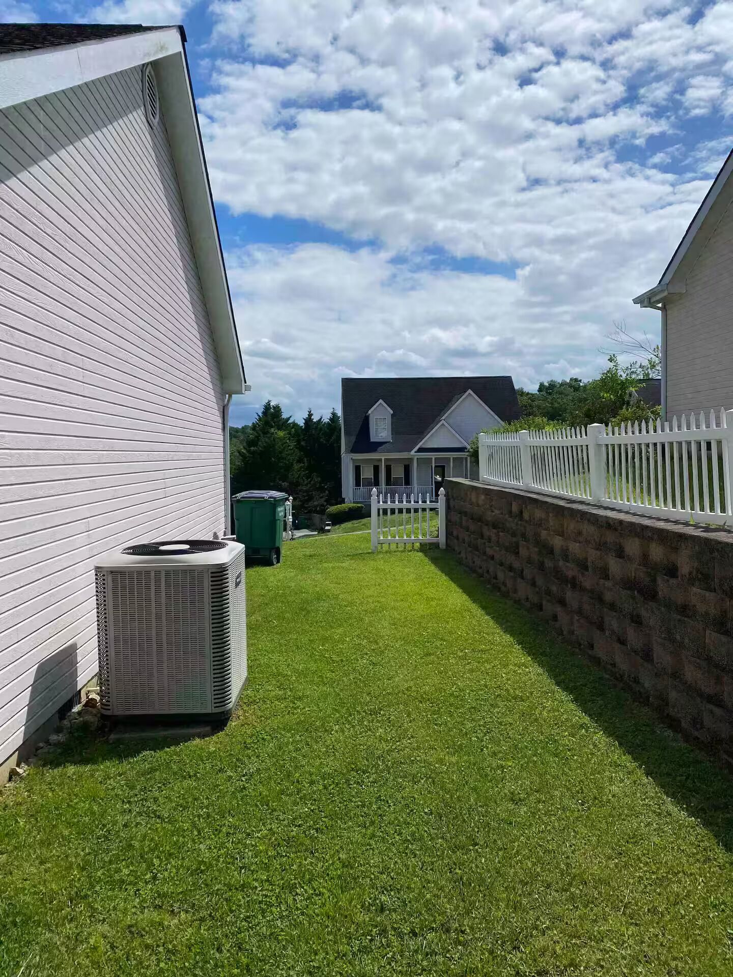 A residential property with a well-maintained lawn, a white picket fence, and a house with a dark roof.