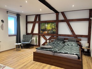 A modern bedroom with a wooden bed, a grey chair, a small table, and a painting on the wall.
