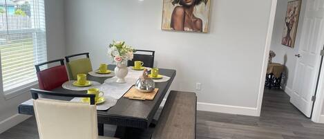 Un coin repas avec une table dressée pour quatre personnes, des chaises, un banc et un tableau accroché au mur.