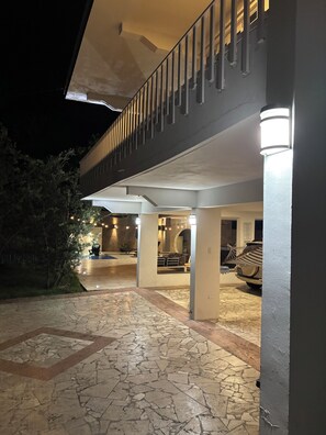 Ein überdachter Außenbereich mit Steinboden, ein Balkon mit Geländern und ein geparktes Auto.