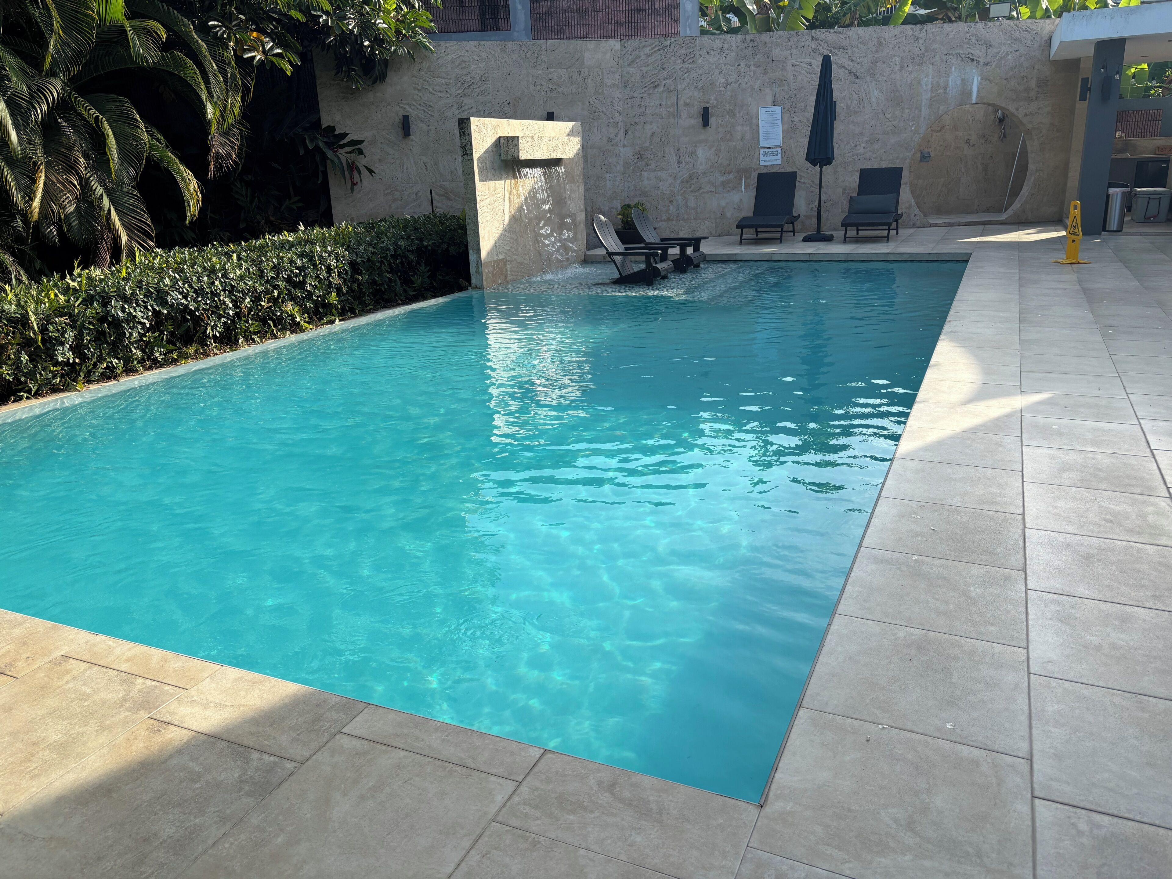 A clear swimming pool with a stone wall and lounge chairs.