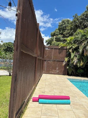 A wooden fence with a pool and two colorful mats on the ground.