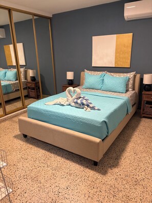 Une chambre à coucher comprenant un lit, des tables de chevet, un miroir et un climatiseur fixé au mur.