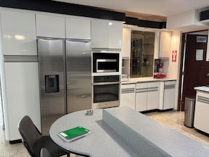 A modern kitchen with stainless steel appliances, a microwave, and a glass display cabinet.