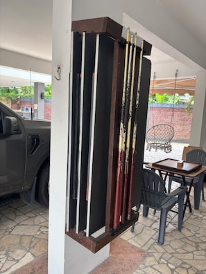 A room with a car parked outside, a table with chairs, and a window overlooking a garden.
