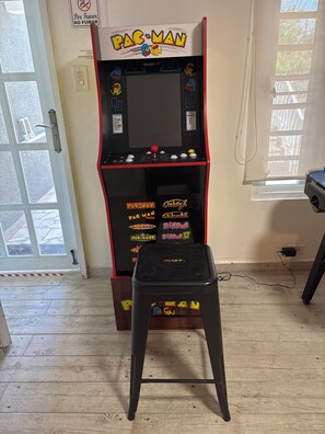 A Pac-Man arcade machine with a stool in front, a door with a sign, and a window with blinds.