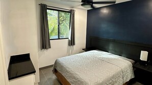 Een slaapkamer met een bed, een plafondventilator, een raam met gordijnen en een klein nachtkastje.