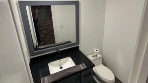 Een moderne badkamer met een wit wastafel, een grote spiegel, een toilet en een handdoekhouder.