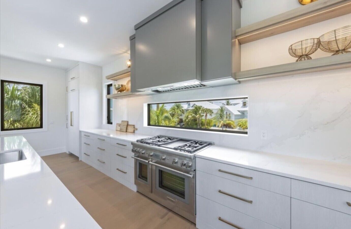 Een moderne keuken met een centraal eiland, roestvrijstalen apparatuur en een raam met uitzicht op groen.