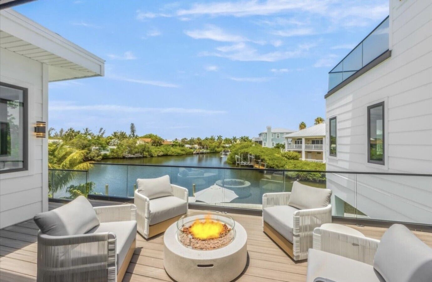 A modern outdoor deck with a fire pit, seating, and a view of a lake and buildings.