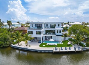 Ein modernes, zweistöckiges Haus mit Pool, umgeben von Palmen und einem Steg.