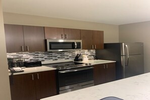 A kitchen with dark wooden cabinets, a stainless steel microwave, a refrigerator, a stove, and a tiled backsplash. - Outstanding apartment at Dawn Beach Club, JW Marriott Resort, Beach and Spa (oyster pond)