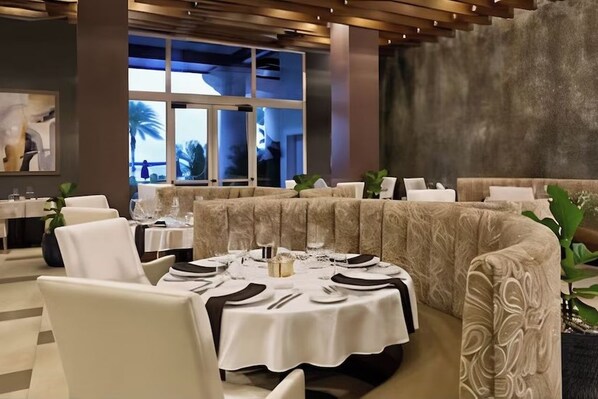 Un ristorante con tavoli rotondi apparecchiati per la cena, vista sull'esterno e un design d'interni moderno.