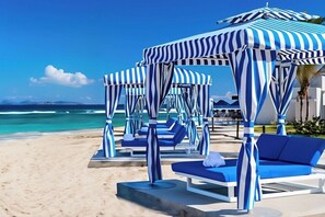 A beachside resort with striped canopies, lounge chairs, and a view of the ocean. - Outstanding apartment at Dawn Beach Club, JW Marriott Resort, Beach and Spa (oyster pond)