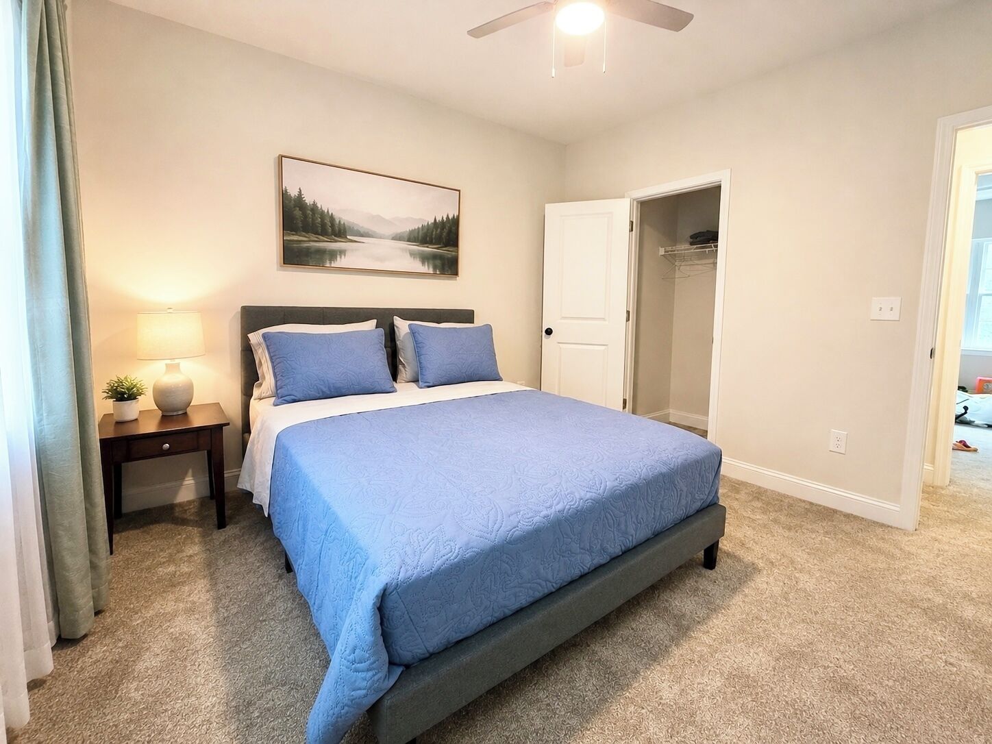 A bedroom with a bed, a nightstand, a lamp, a painting, and a closet.