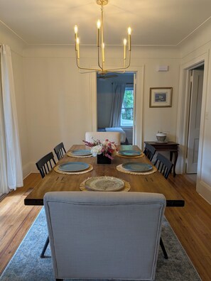 A dining room with a wooden table set for four, surrounded by chairs, a chandelier, and a vase with flowers.