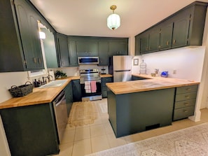 A kitchen with dark cabinets, stainless steel appliances, a wooden countertop, and a small rug on the floor.