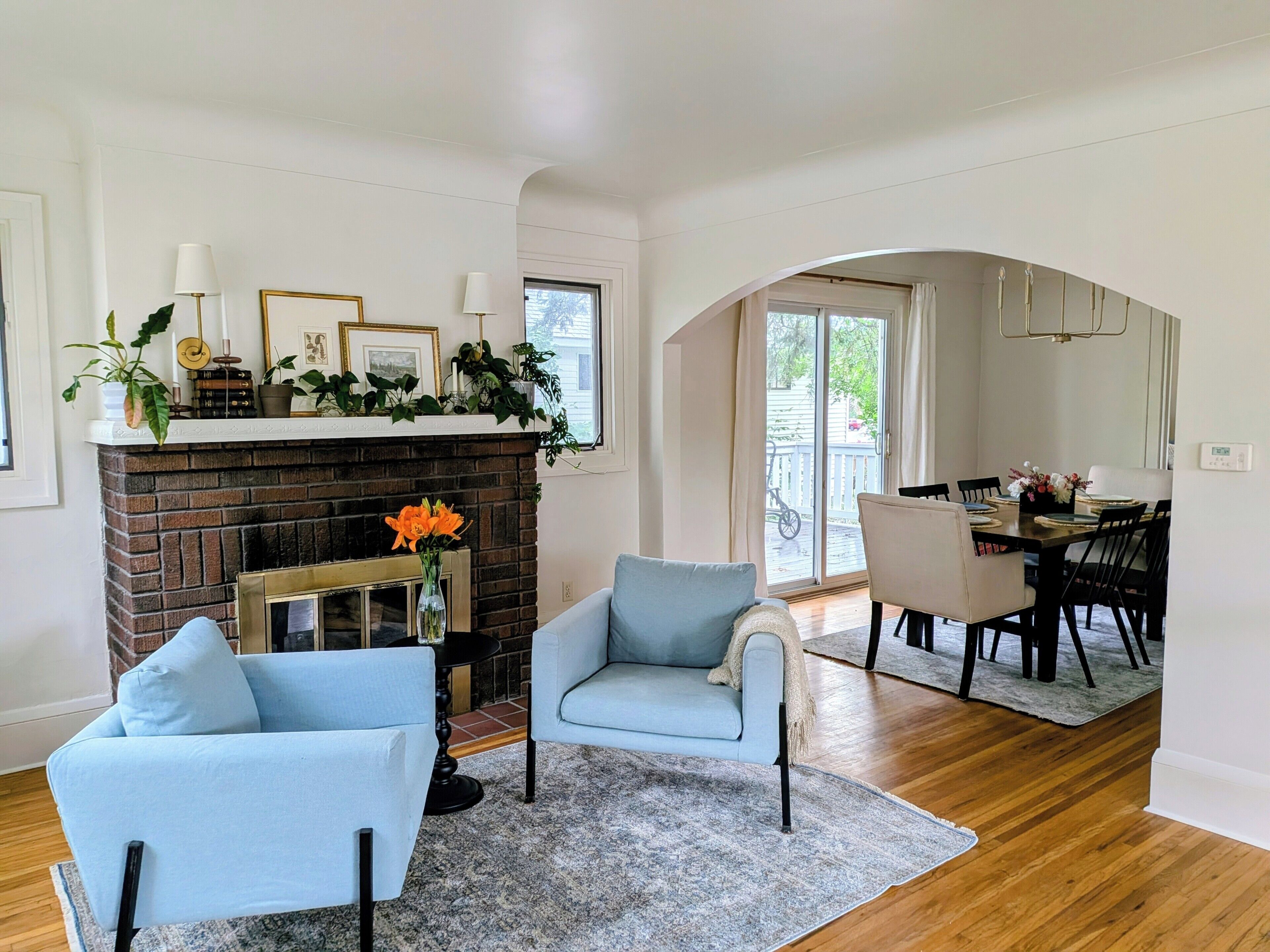 Un salon doté d’une cheminée, de deux fauteuils, d’un coin repas avec une table et des chaises, et d’une vue sur l’extérieur par le biais d’une arche.
