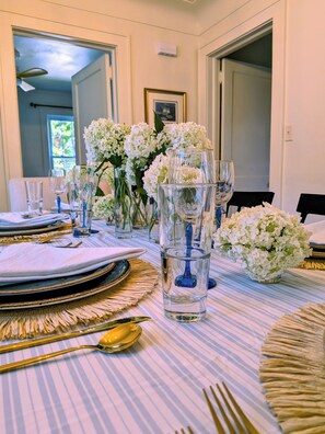 A dining table set with plates, glasses, and cutlery, surrounded by white flowers and a vase.