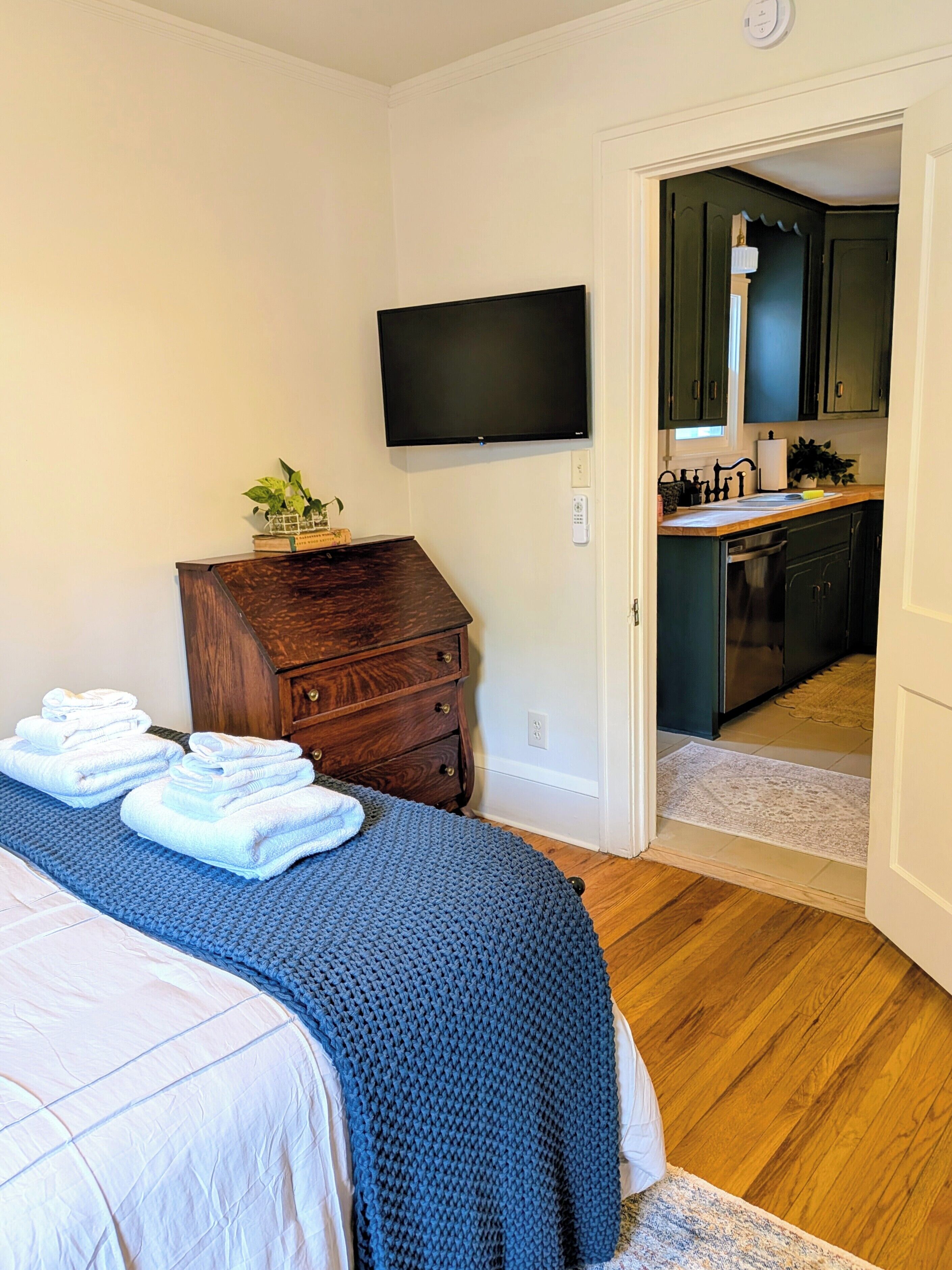 Un dormitorio con una cama, un aparador de madera, un televisor y vistas hacia una zona de cocina.