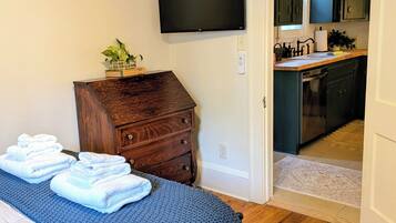 Un dormitorio con una cama, un aparador de madera, un televisor y vistas hacia una zona de cocina.