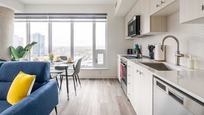 Eine moderne Küche mit einem großen Fenster, weißen Schränken und einem blauen Sofa mit einem gelben Kissen.