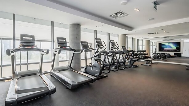 Ein Fitnessstudio mit Laufbändern, Crosstrainern und einem Fernsehbildschirm.