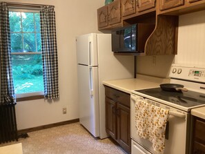 A kitchen with a refrigerator, microwave, stove, and a window with curtains.