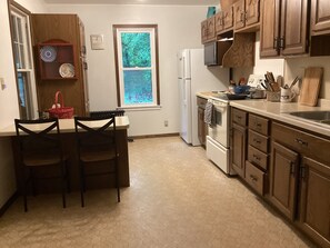 A kitchen with a dining table, chairs, a refrigerator, a stove, and wooden cabinets.