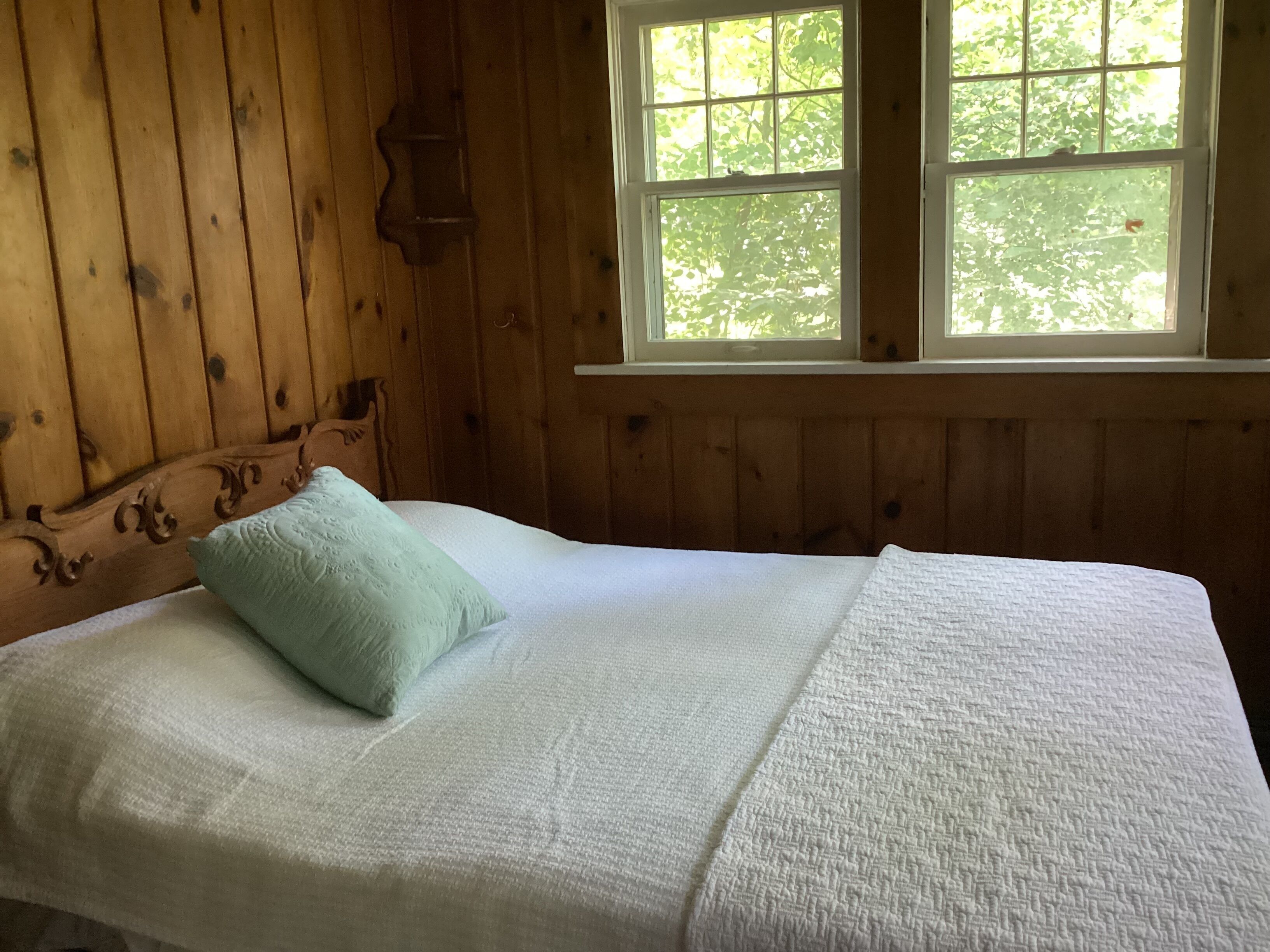A wooden cabin room with a bed, a window, and a wall-mounted shelf.