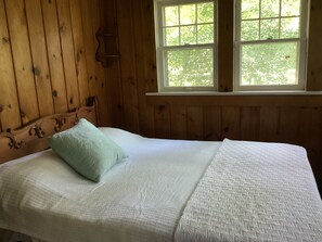 Habitación tipo cabaña de madera con una cama, una ventana y una repisa en la pared.