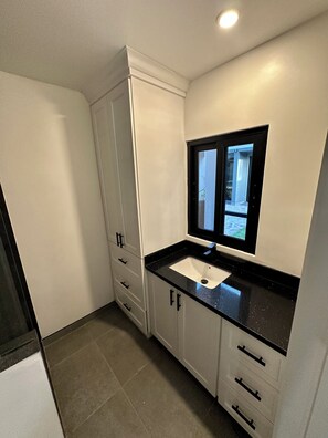 Ein modernes Badezimmer mit einem weißen Waschtisch, einer schwarzen Arbeitsplatte und einem Fenster über dem Waschbecken.