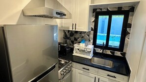 Cocina compacta con refrigerador de acero inoxidable, estufa a gas, gabinetes blancos y encimera negra.
