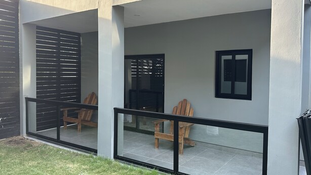 Un edificio moderno con balcón de vidrio, sillas de madera y una mesa pequeña.