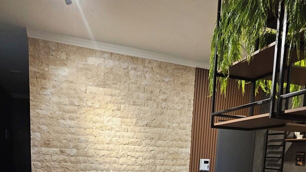 Ein Essbereich mit Steinwand, Holztisch und -stühlen sowie einer Küchenzeile mit Pflanze.