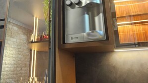 Ein modernes Interieur mit Glastrennwand, einem an einer Holzplatte montierten Flachbildfernseher und einem Tisch mit Gläsern und einer Kerze.