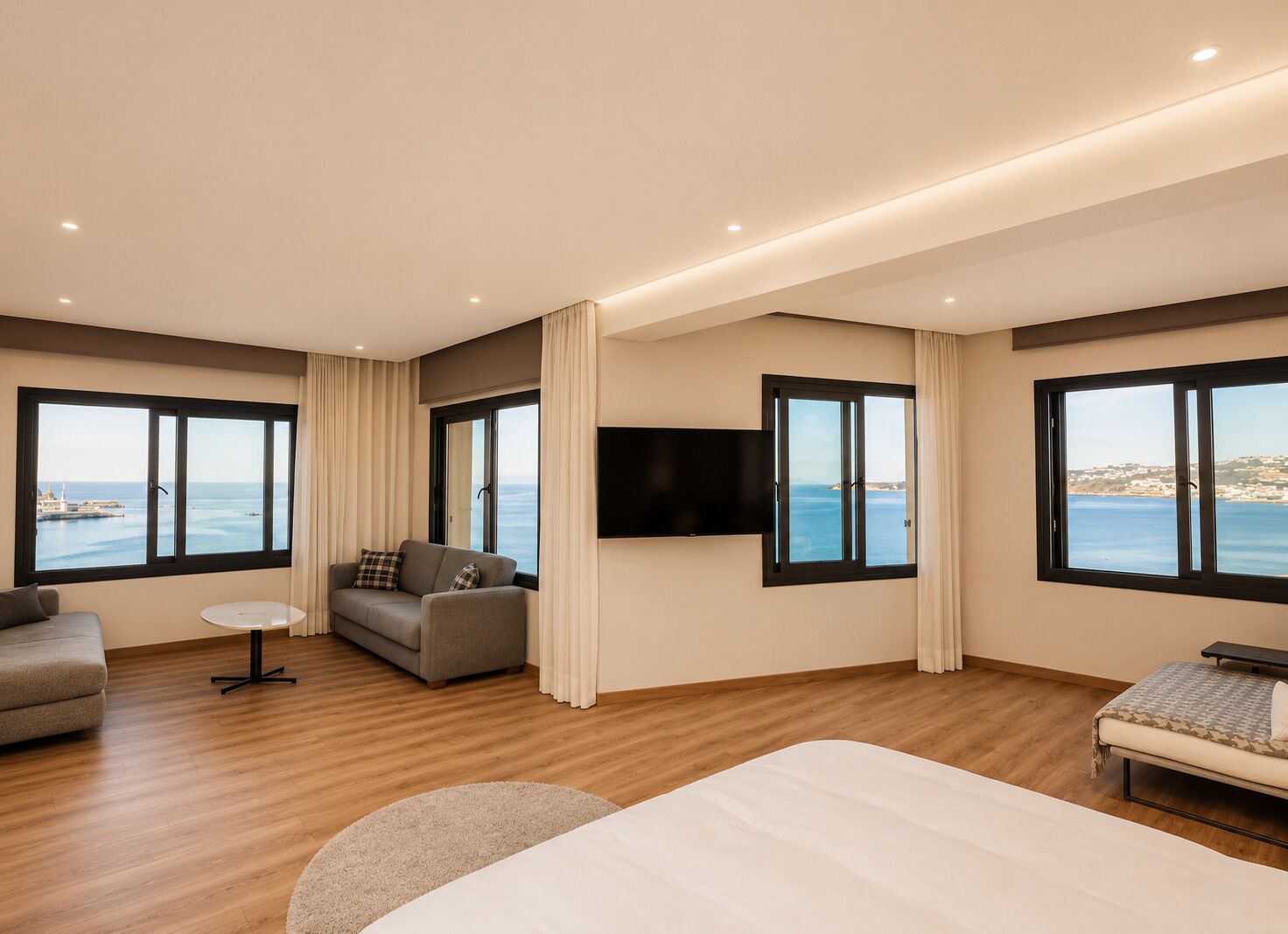 Een hotelkamer met een groot bed, een sofa, een klein tafeltje en een televisie. Er zijn grote ramen met uitzicht op de zee.