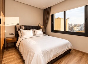 Une chambre d’hôtel avec un grand lit, une table de chevet, une fenêtre donnant sur la ville et un rideau.