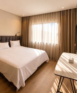 Ein Hotelzimmer mit einem großen Bett, einem Nachttisch, einer Kopfteil und einem Fenster mit Vorhängen.