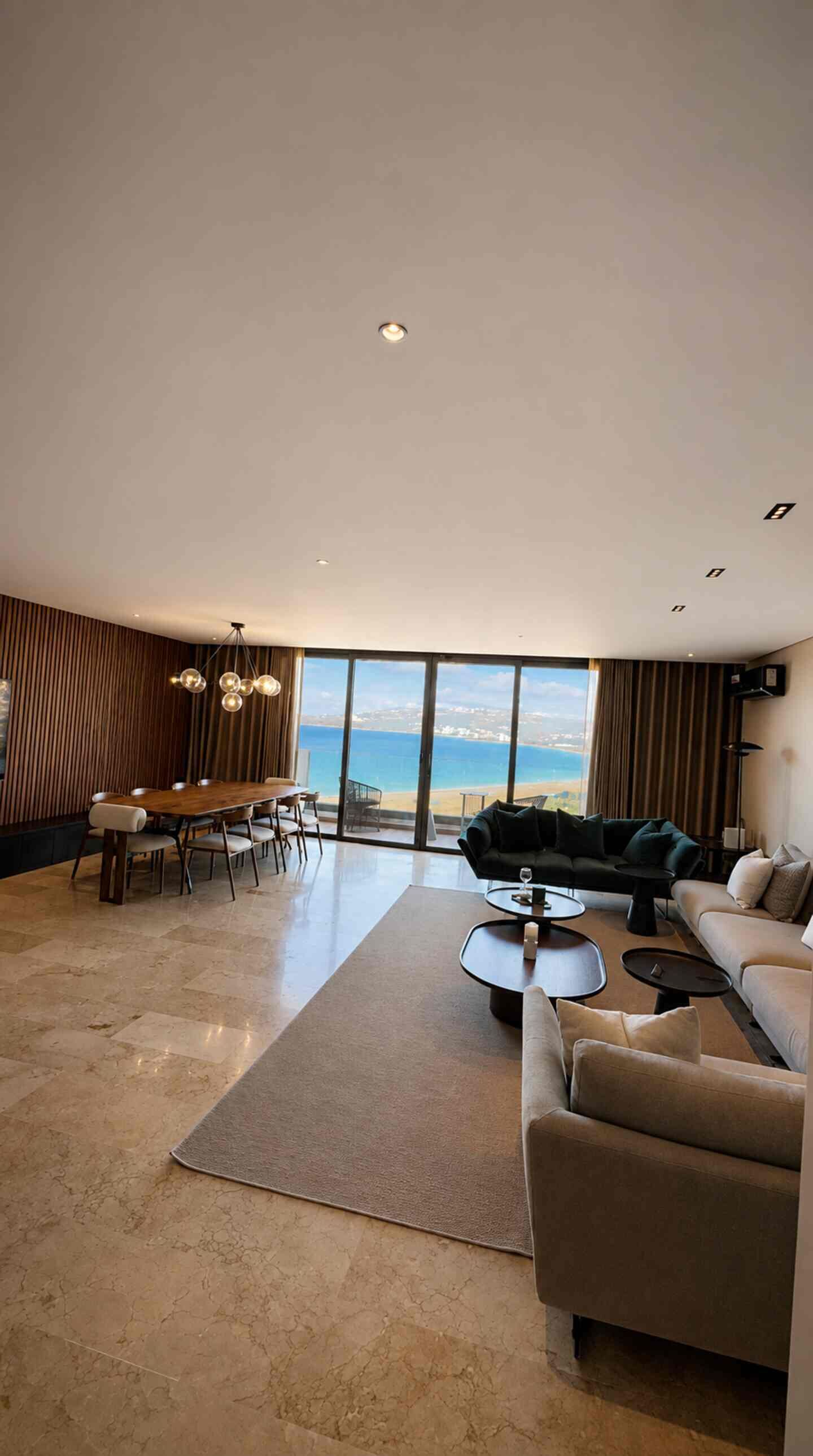 Un vaste espace de vie comprenant un grand salon avec une grande fenêtre donnant sur la plage, une table à manger et un canapé.