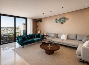 A modern living room with a large window, a teal sofa, a grey sofa, and a round coffee table. - Exclusive apartment with stunning panoramic sea views (Tanger)